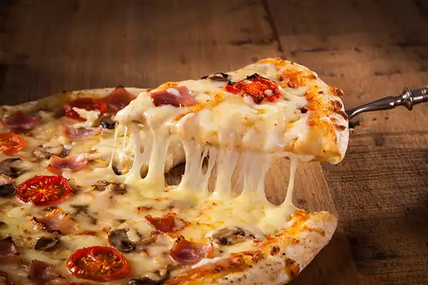 Slice of hot pizza with melting cheese on rustic wooden table.