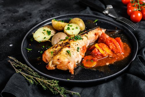 Baked in tomatoes monkfish with potatoes and vegetables. Black background. Top view