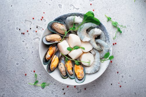 Mixed frozen seafood in plate on a gray stone background. Raw Shrimp, mussels and scallops